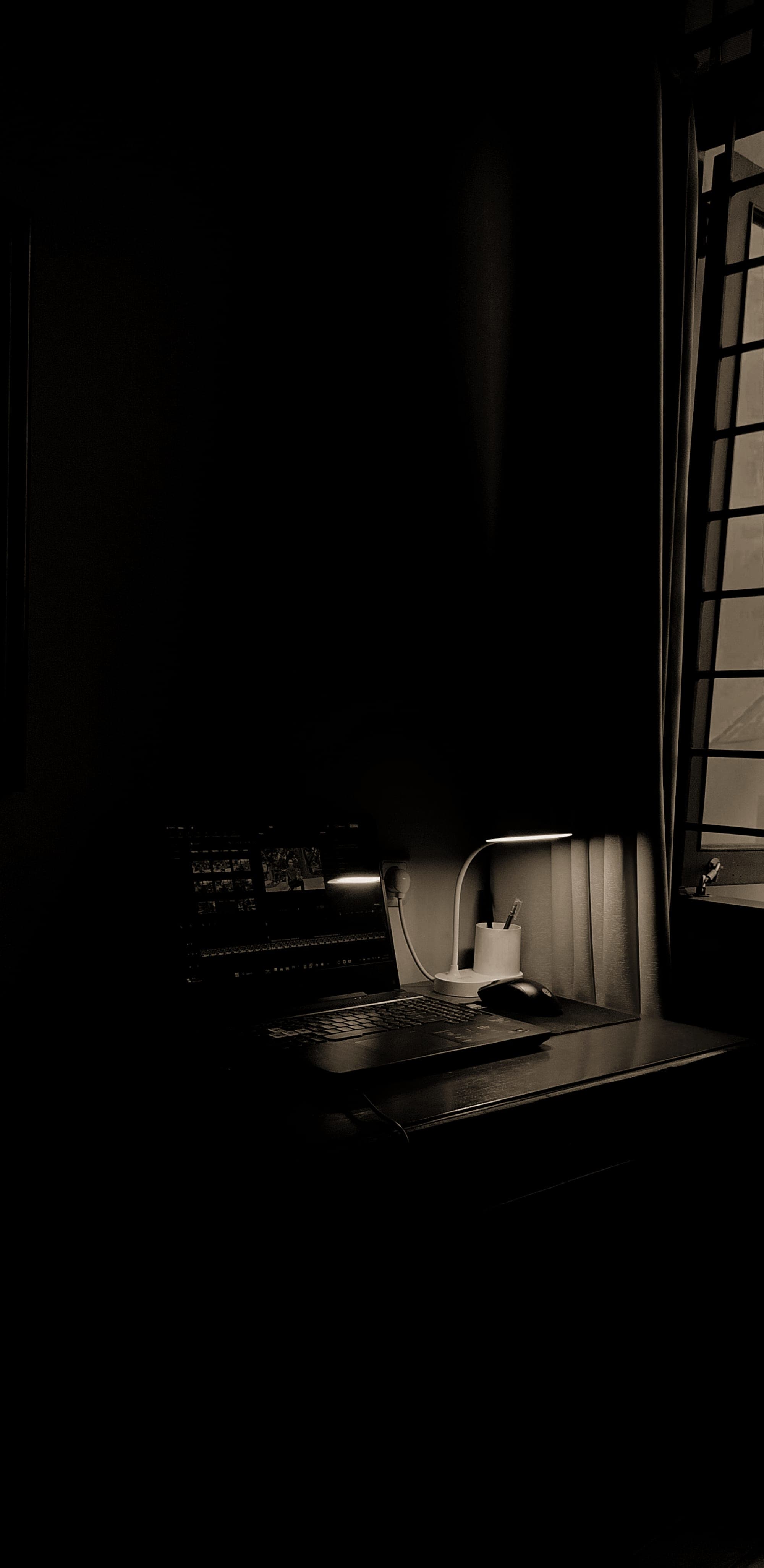 A desk with a lamp left on in a dark room