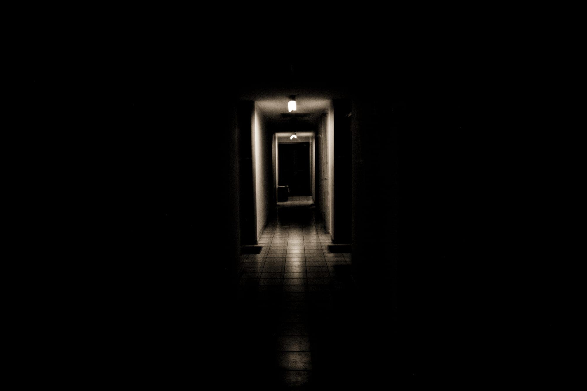 A single lit doorway at the end of a dark hall