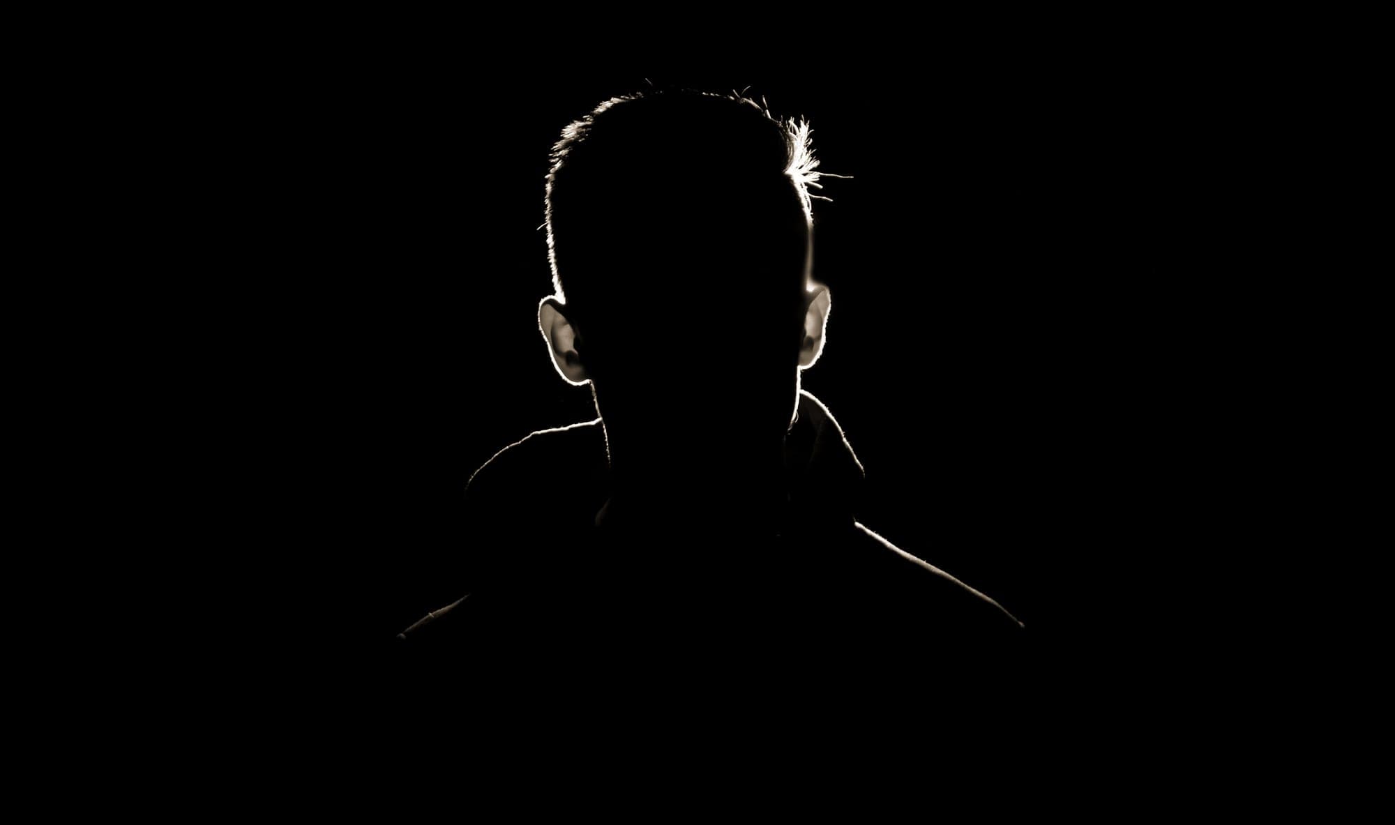 A man lit only along the edge of his shoulders
